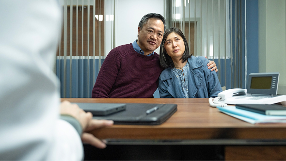 Man in orange shirt talking with a man in a white room