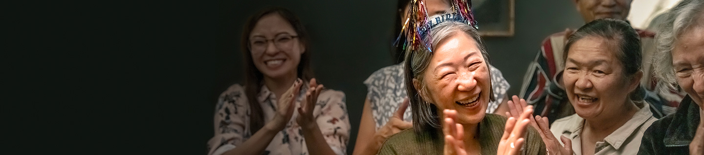 Elderly woman celebrating her birthday with people clapping around her
